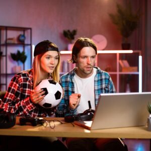 Worried young man and woman watching soccer game on wireless laptop at home.