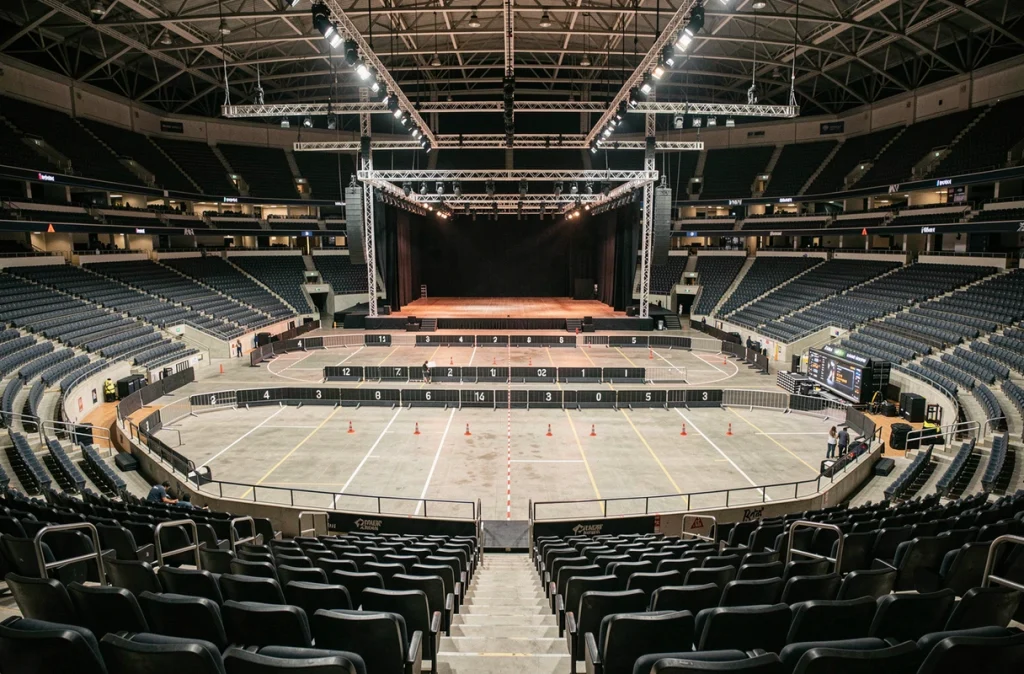 Vue en plongée des tribunes et de la fosse d'une grande salle de concert intérieure type Bercy Arena avec scène vide